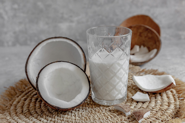 glass of coconut milk next to a cut open coconut