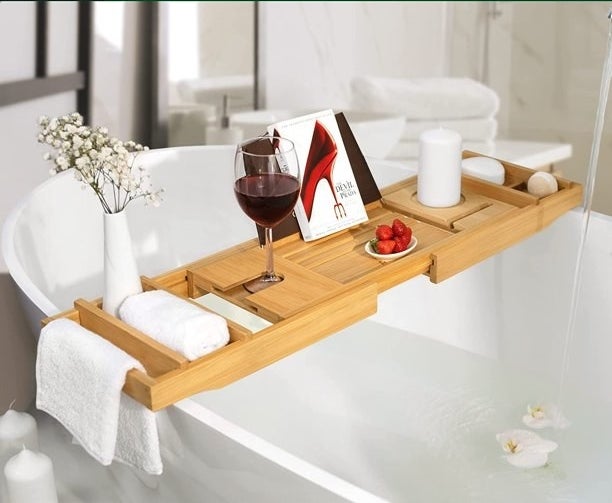 the bamboo bath caddy with towels, a book, a glass of wine, a bowl of strawberries, flowers and a candle on it