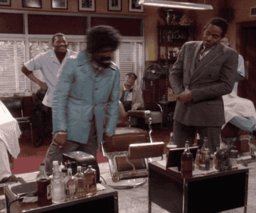 Man with an afro dancing in a barbershop with men in the background