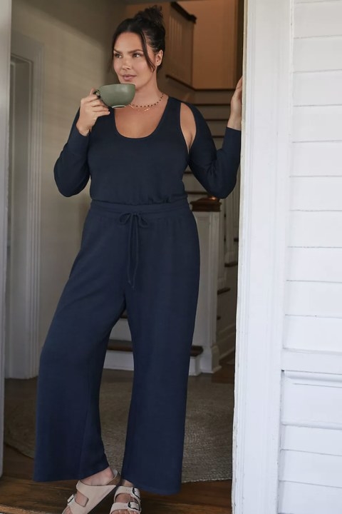 Model wearing black jumpsuit with matching shrug, sipping out of mug