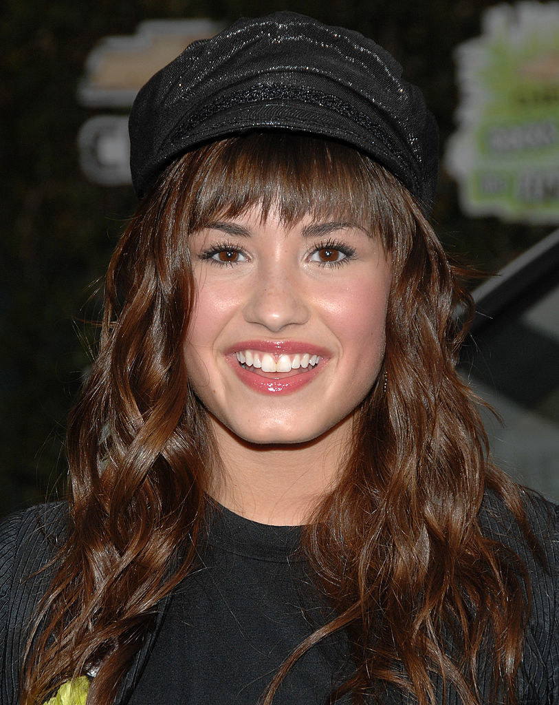 Demi with bangs and wavy hair under a newsboy cap