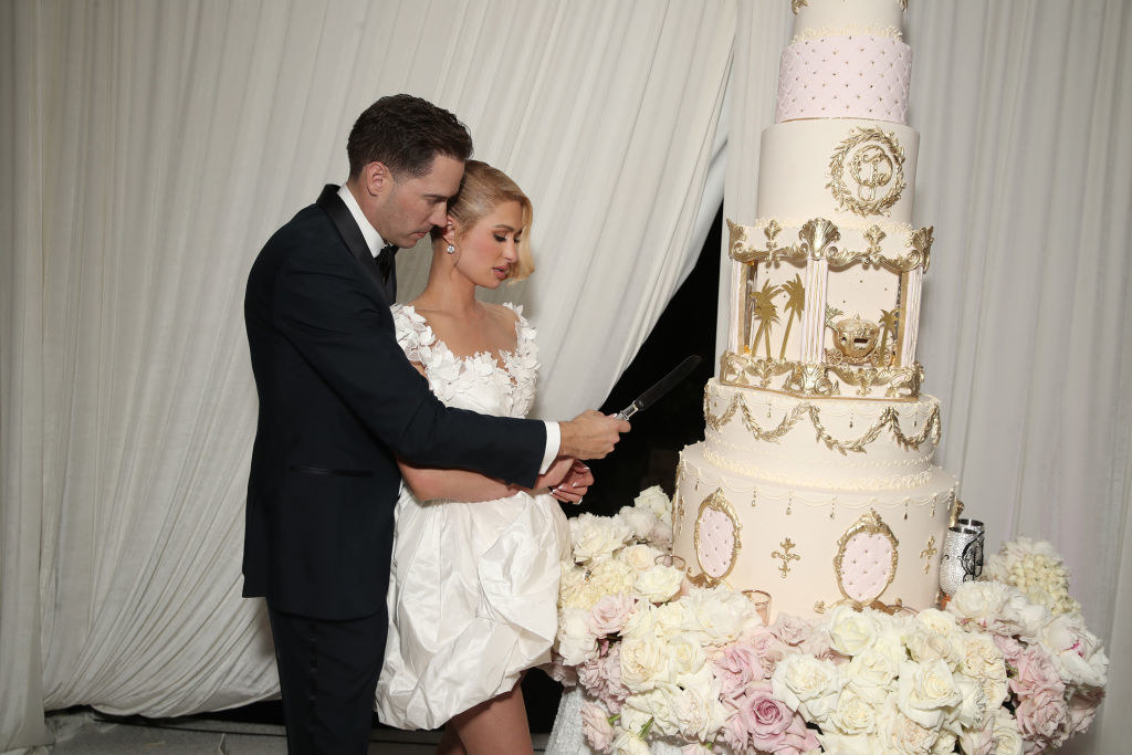 Carter standing behind Paris and holding a knife and preparing to cut a huge, tiered wedding cake