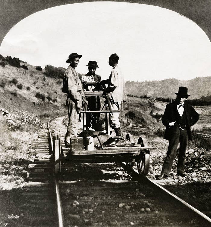 an old photo of three Black kids working on the railroad while a white business guy stands on the side
