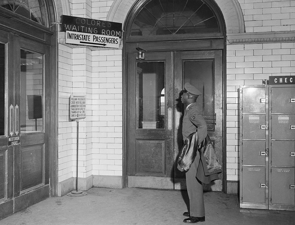 a Black man standing outside doors with various signs on them