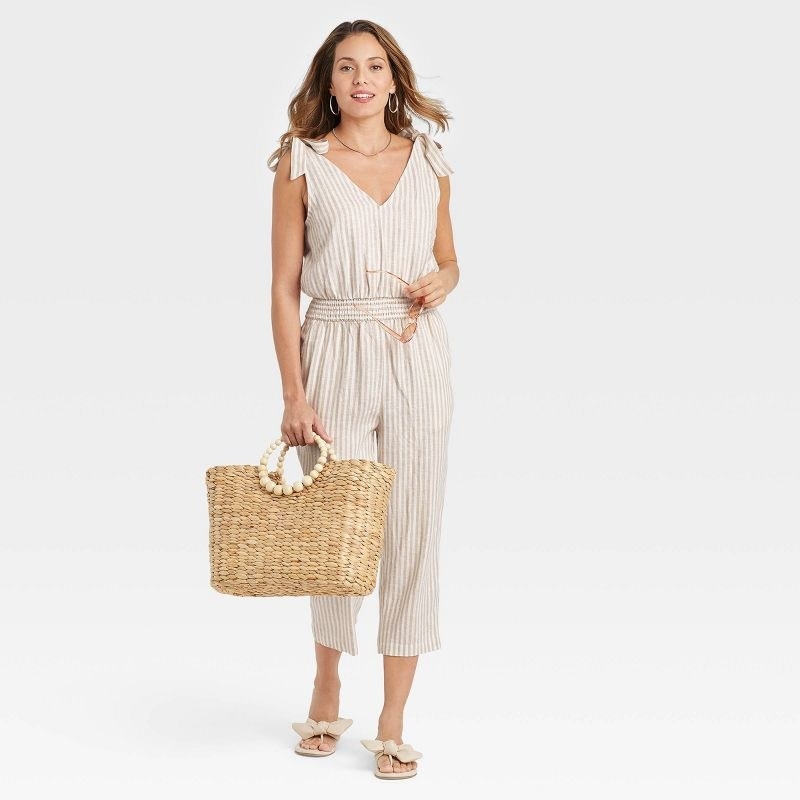model wearing the cream striped jumpsuit with straw tote bag
