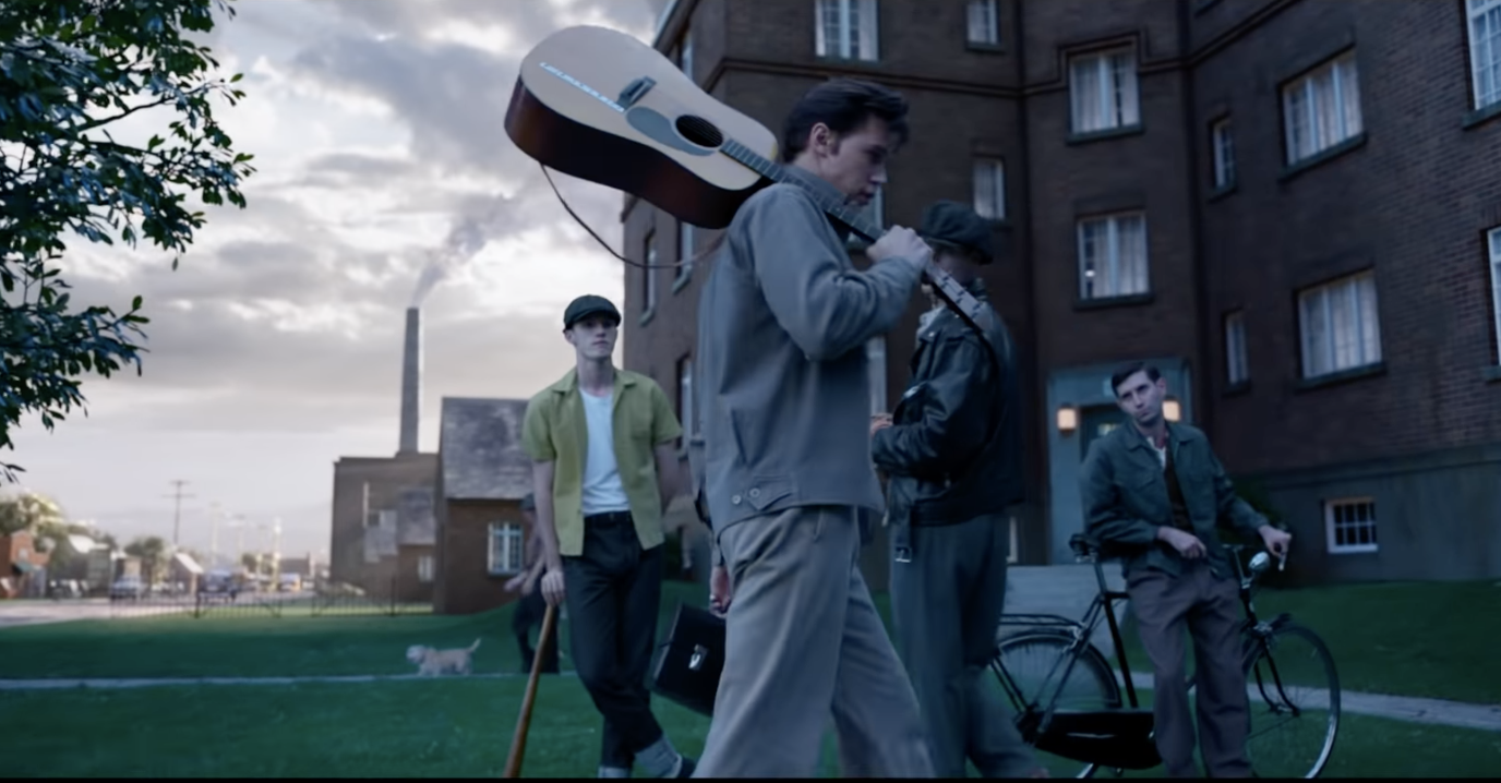 Austin Butler as Elvis carries an acoustic guitar