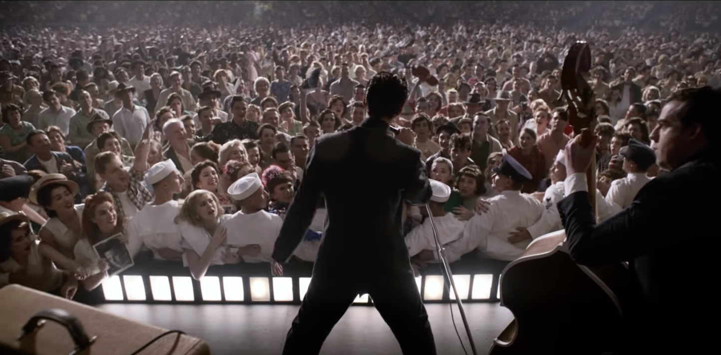 A still from the movie Elvis shows Austin Butler as Elvis performing to a massive crowd