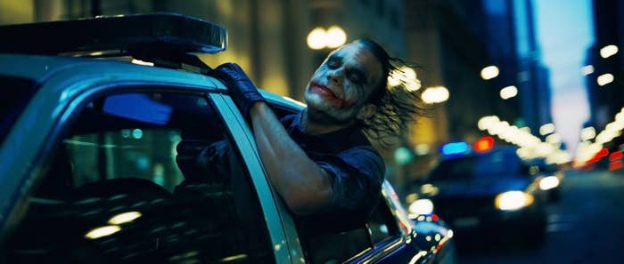 The Joker hangs out the driver&#x27;s side of a police car
