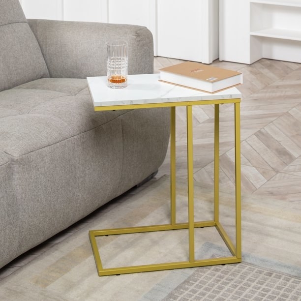 the gold and faux marble end table holding a book and glass in front of a sofa