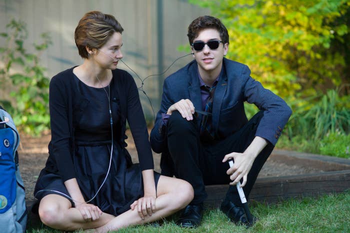 Hazel Grace and Isaac sit in the grass while sharing headphones