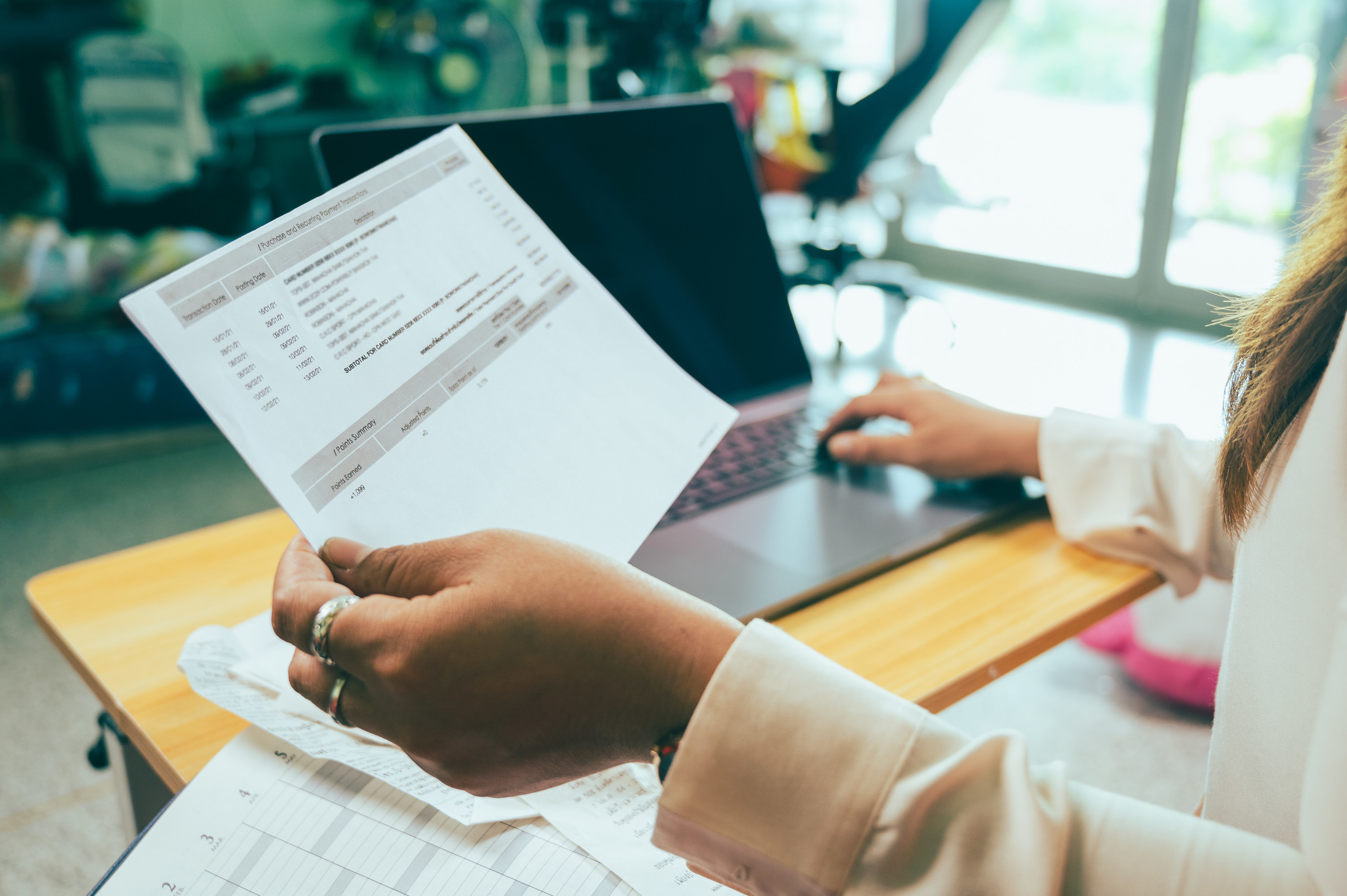 A hand holding up a bill in front of a laptop