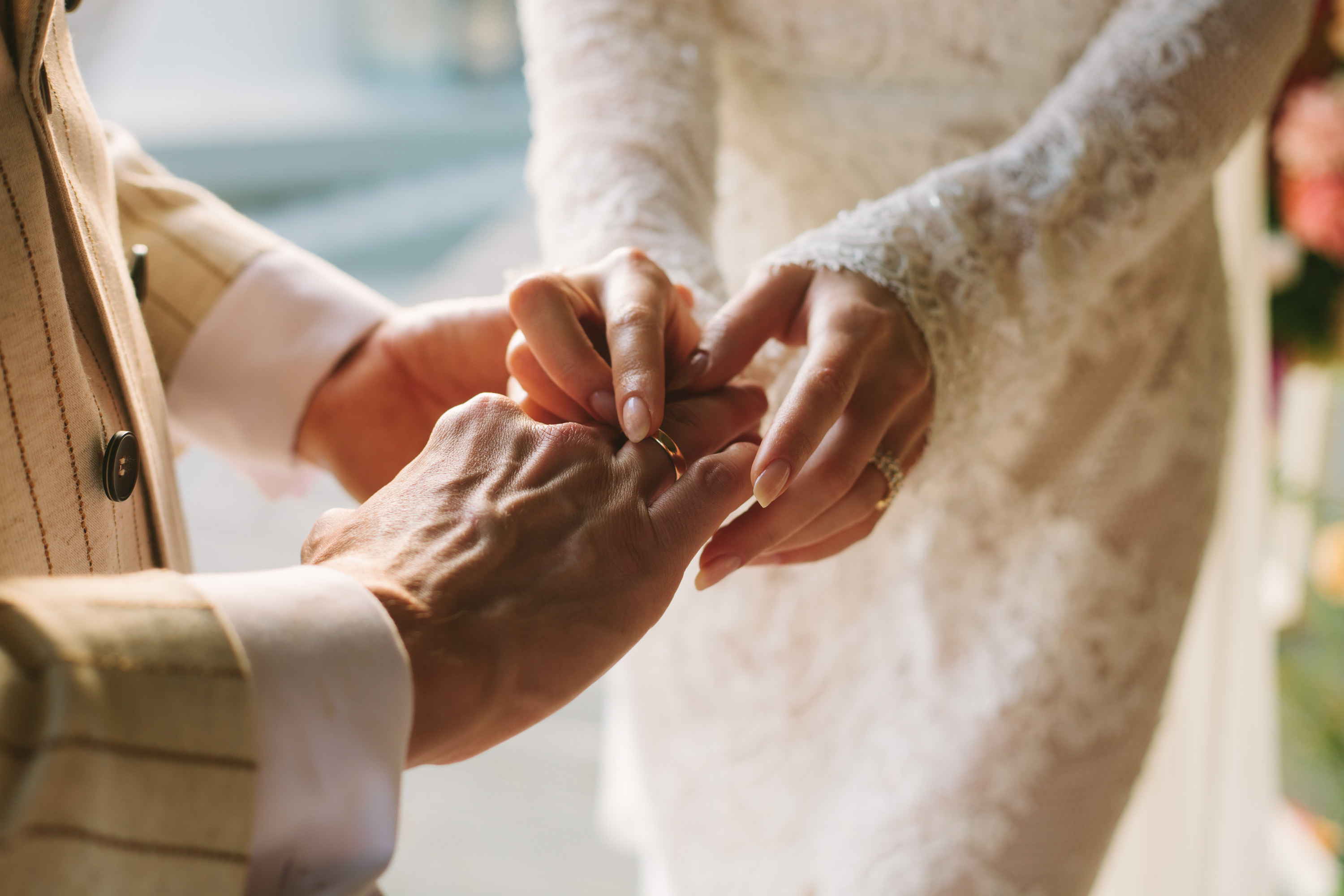 A bride putting a wedding band onto her groom&#x27;s finger