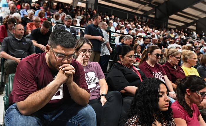 An audience sits in bleachers, many wearing the color maroon and bowing their heads in prayer