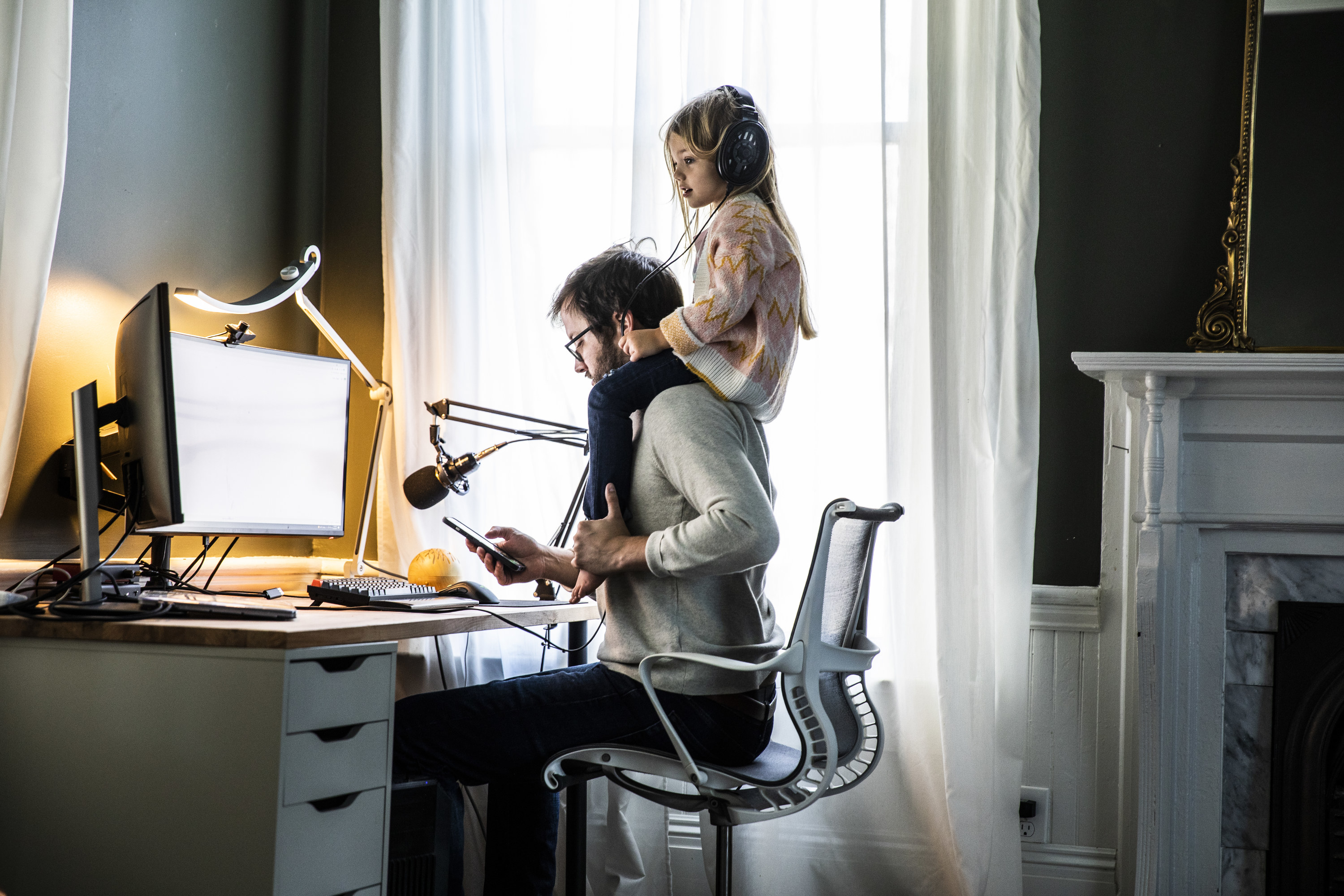 A man working at a home office with his daughter on his shoulders