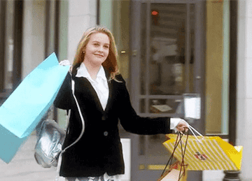 alicia silverstone as cher in clueless walking with a bunch of shopping bags and smiling
