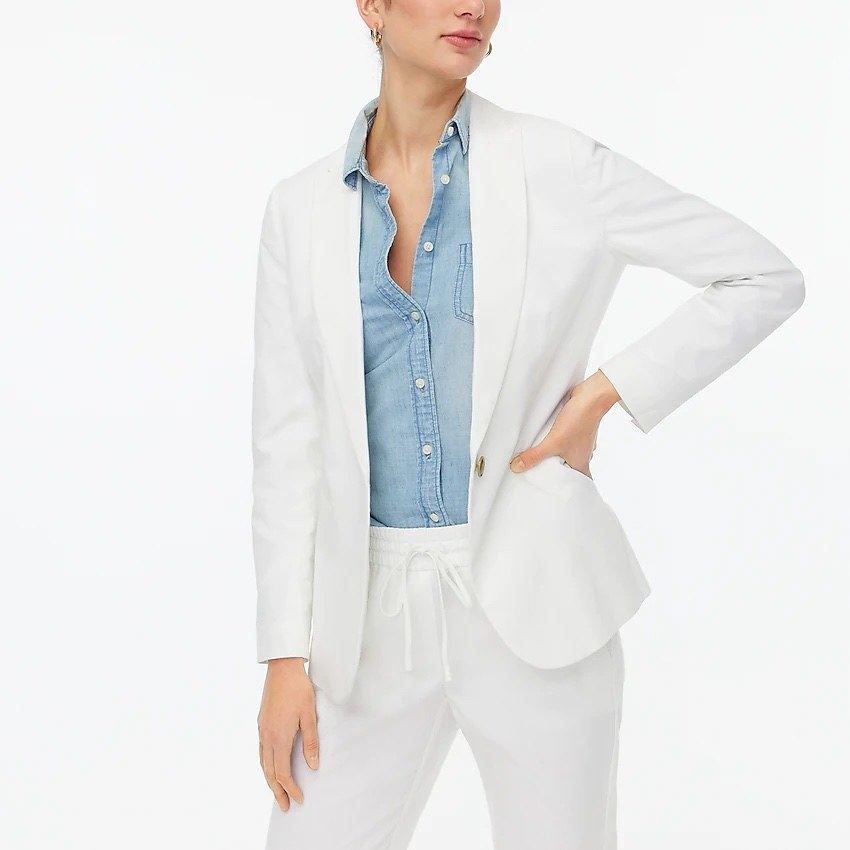 model wearing the white blazer over a denim button down with white pants