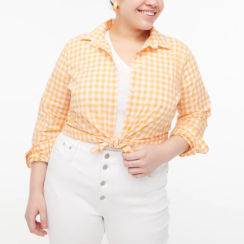 model wearing the orange and white gingham button-down, tied in a knot, with white jeans