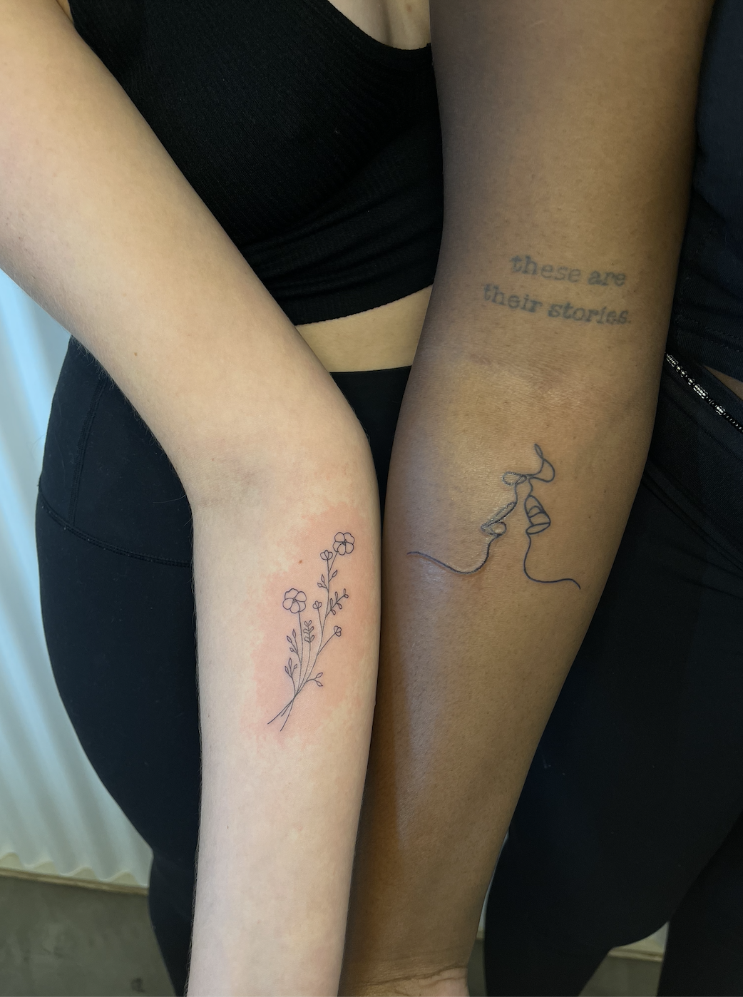 Shelby showing off a floral tat and Ehis showing a line tat of two figures about to kiss