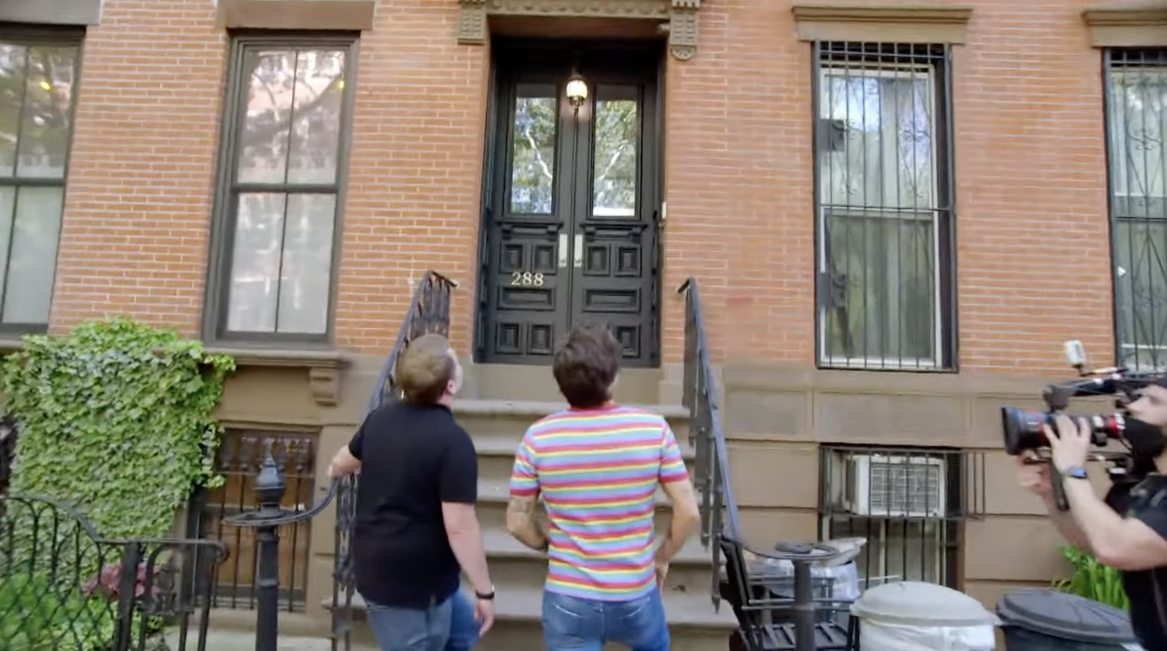 Corden and Styles face a brownstone stoop, looking up at a second-level window