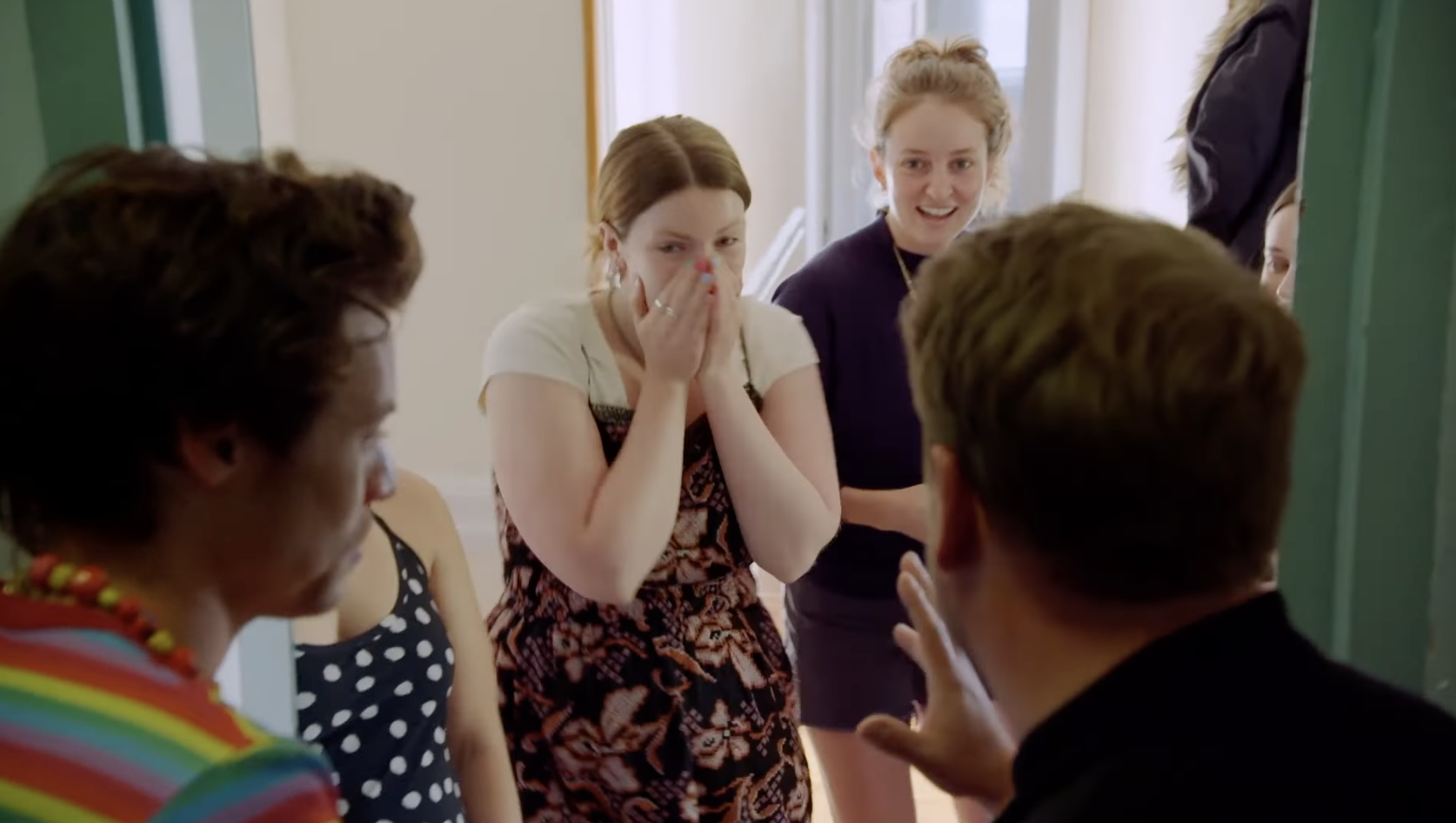 Four women, one with hands covering her mouth, face Corden and Styles standing in the doorway