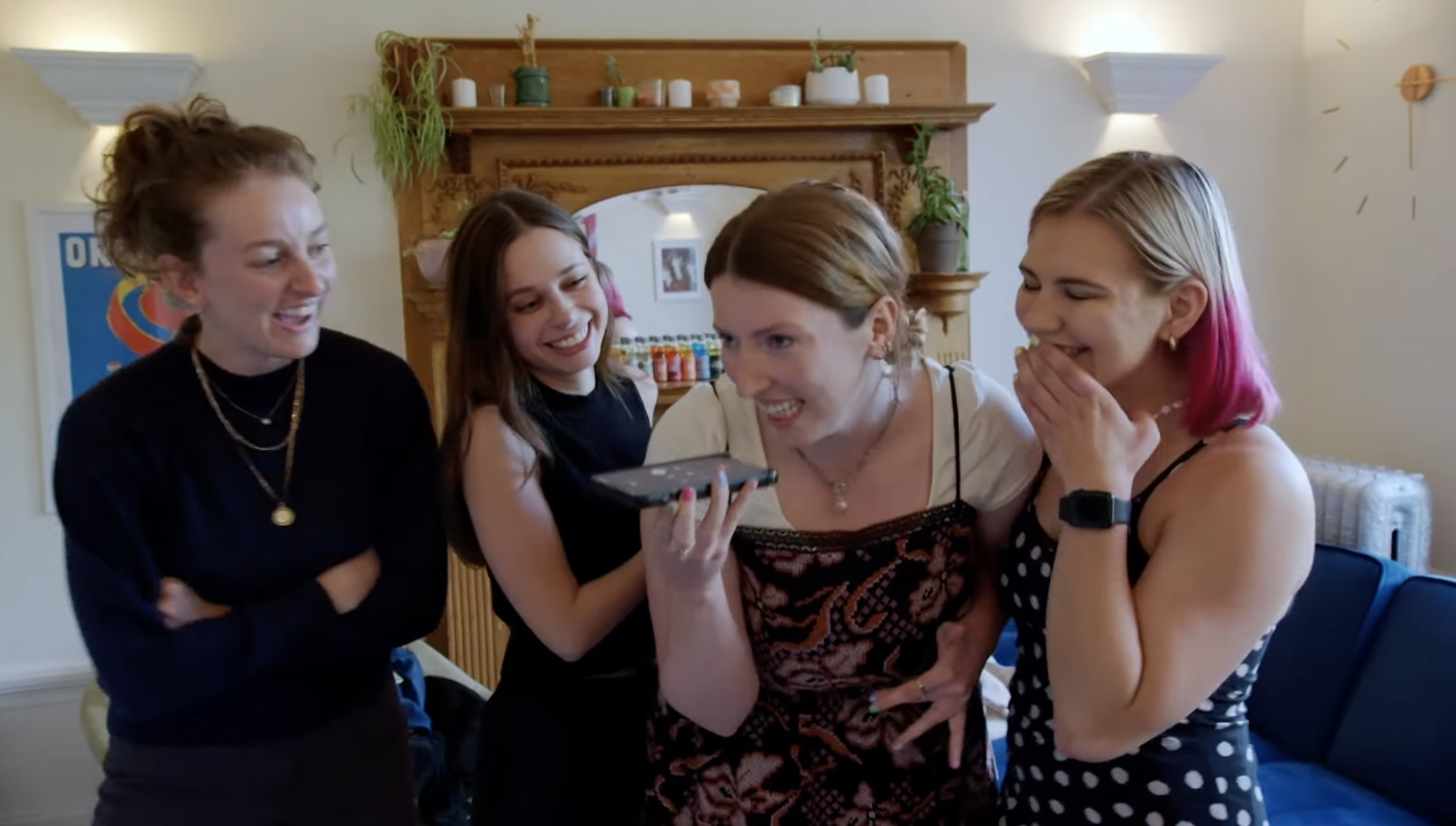 One roommate talks into her phone as her three roommates laugh and stand around her