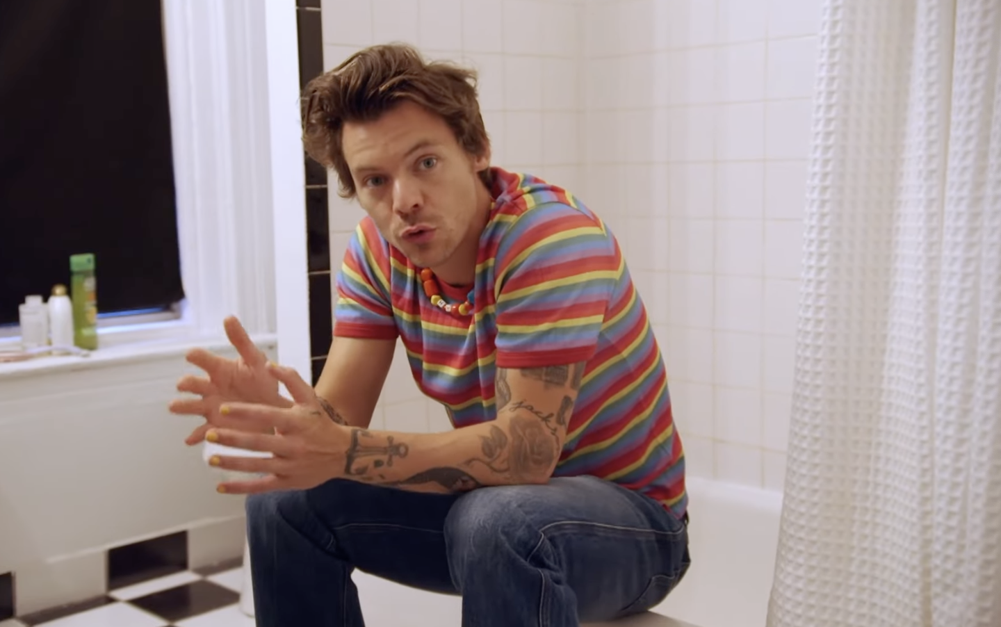 Styles sits on the perch of the tub, talking to the camera