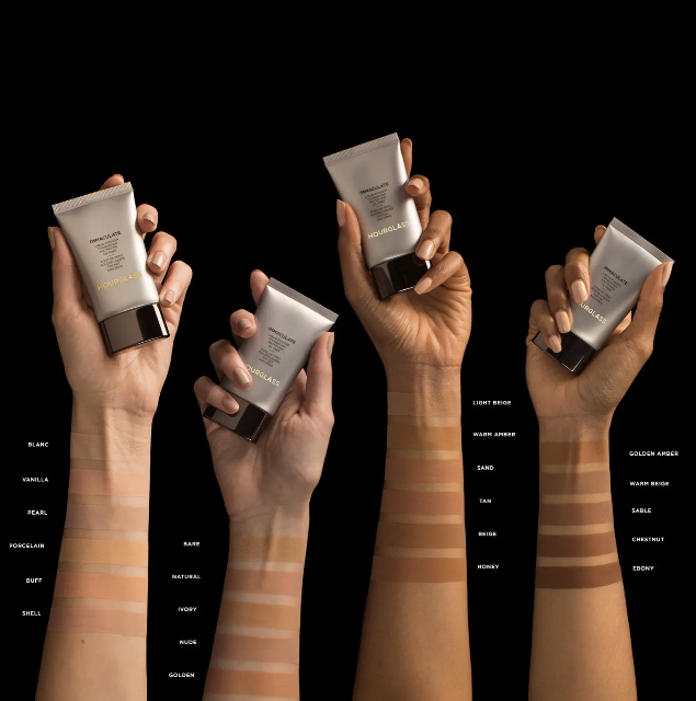 four models&#x27; hands holding tubes of the foundation, with swatches of the different foundation shades on their arms