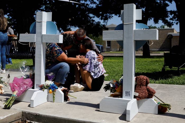 Three people kneel with their heads bowed together by two wooden crosses