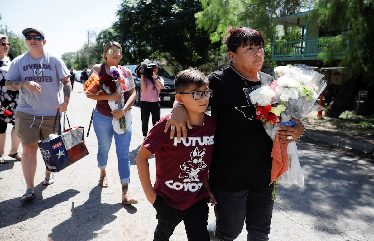 A woman holds a bouquet of flowers and holds an arm around a grandson&#x27;s neck