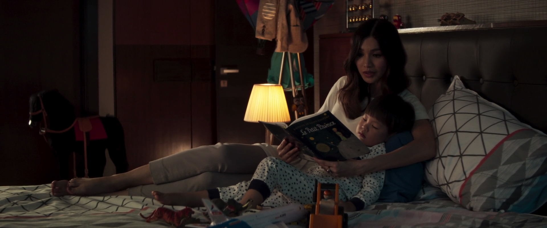 A character reading a book to a child in bed, and neither person has shoes on