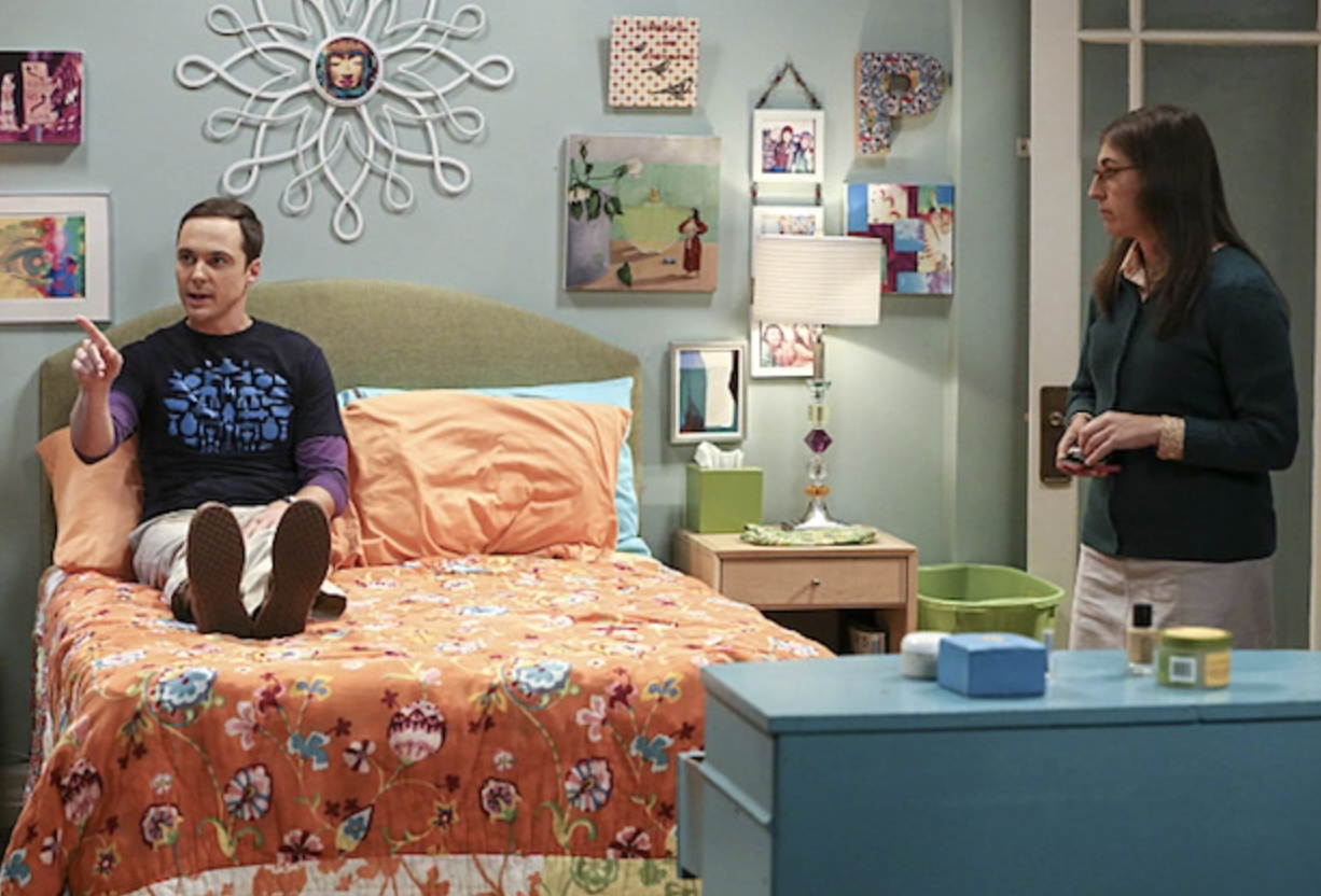 Sheldon sits up in bed while fully clothed and wearing shoes