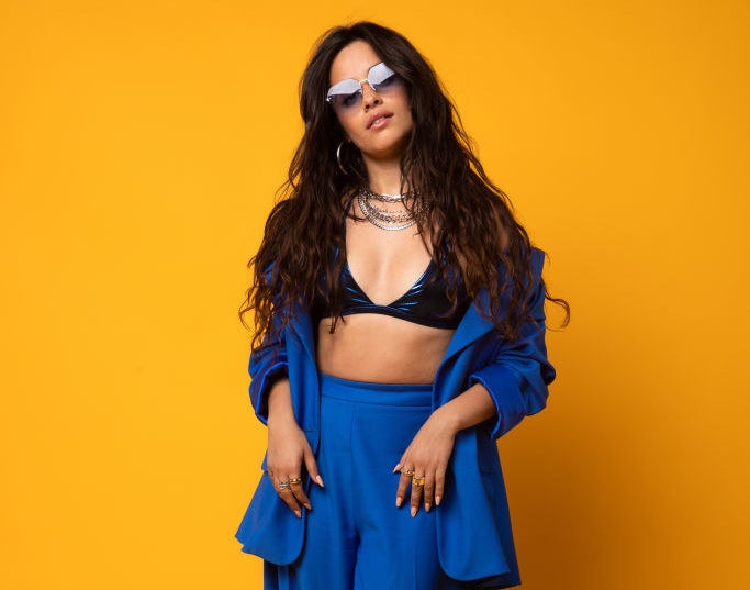 Camila in a blue jacket and dress ensemble and sunglasses