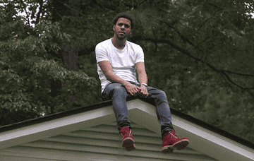 A gif of J. Cole sitting on top of the roof of his childhood home