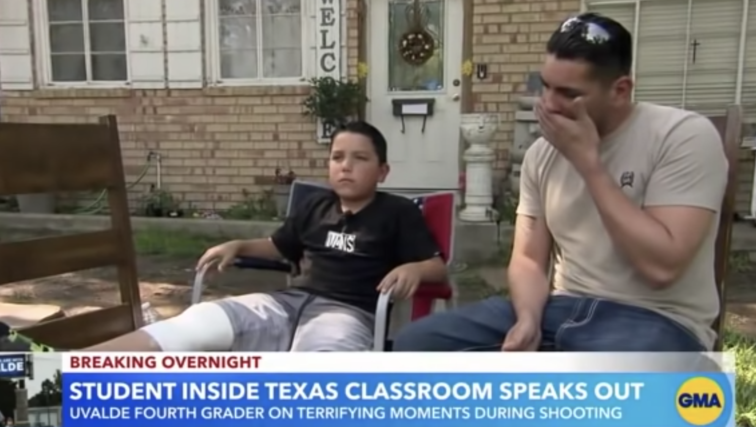 A young boy sitting outside a house next to an older man who has his hand at his mouth