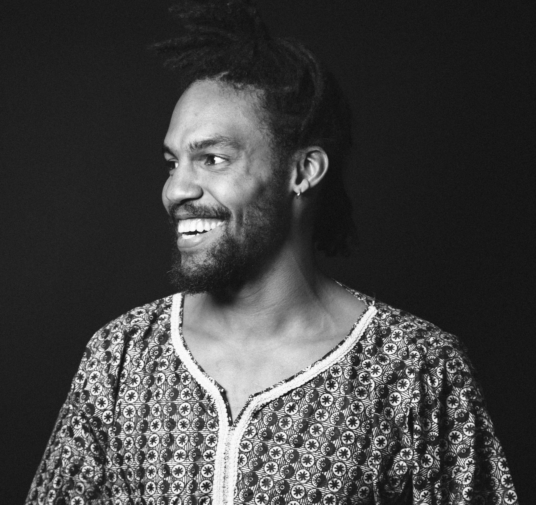Pierce Freelon photographed in black and white, wearing a dashiki and smiling