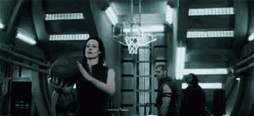 Person holding a basketball, preparing to shoot in a futuristic indoor court with others in the background. Lighting is dramatic