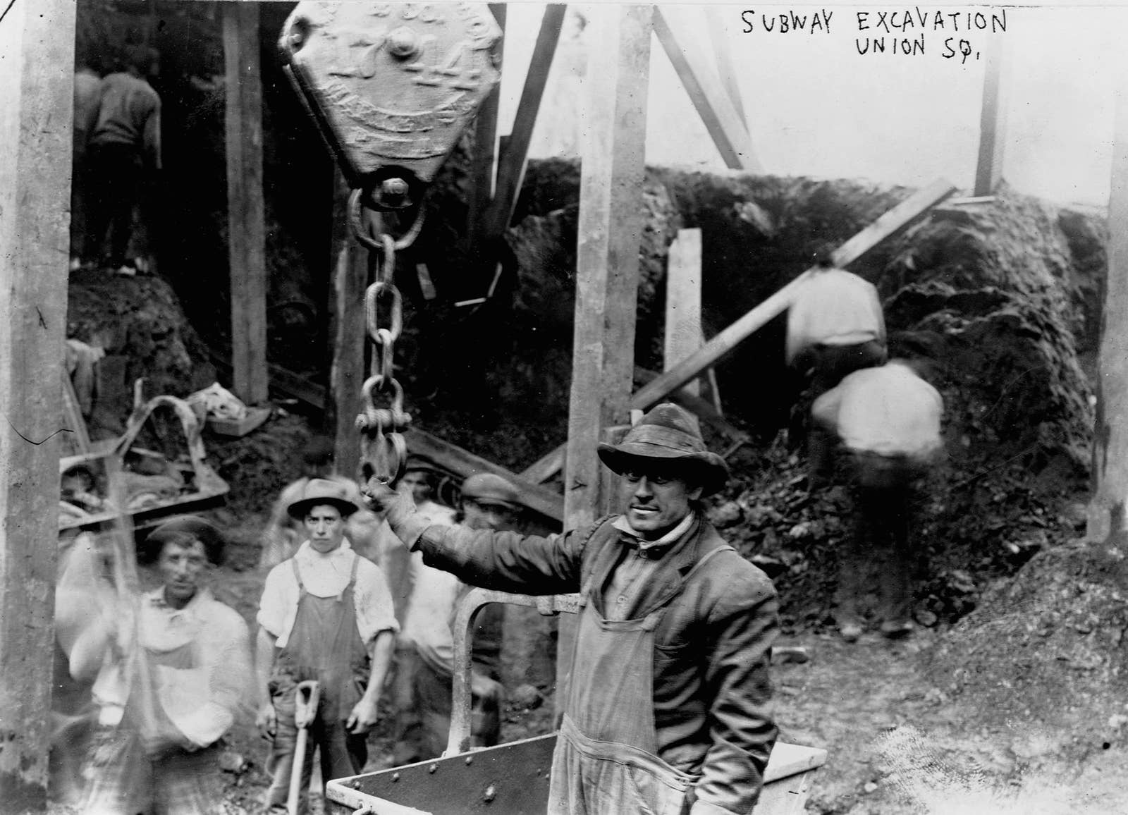 Workers look into camera for a portrait under some scaffolding and construction poles; text reads "subway excavation union square"