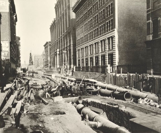 Wide city street is torn up with large metallic pipes and scaffolding placed underground