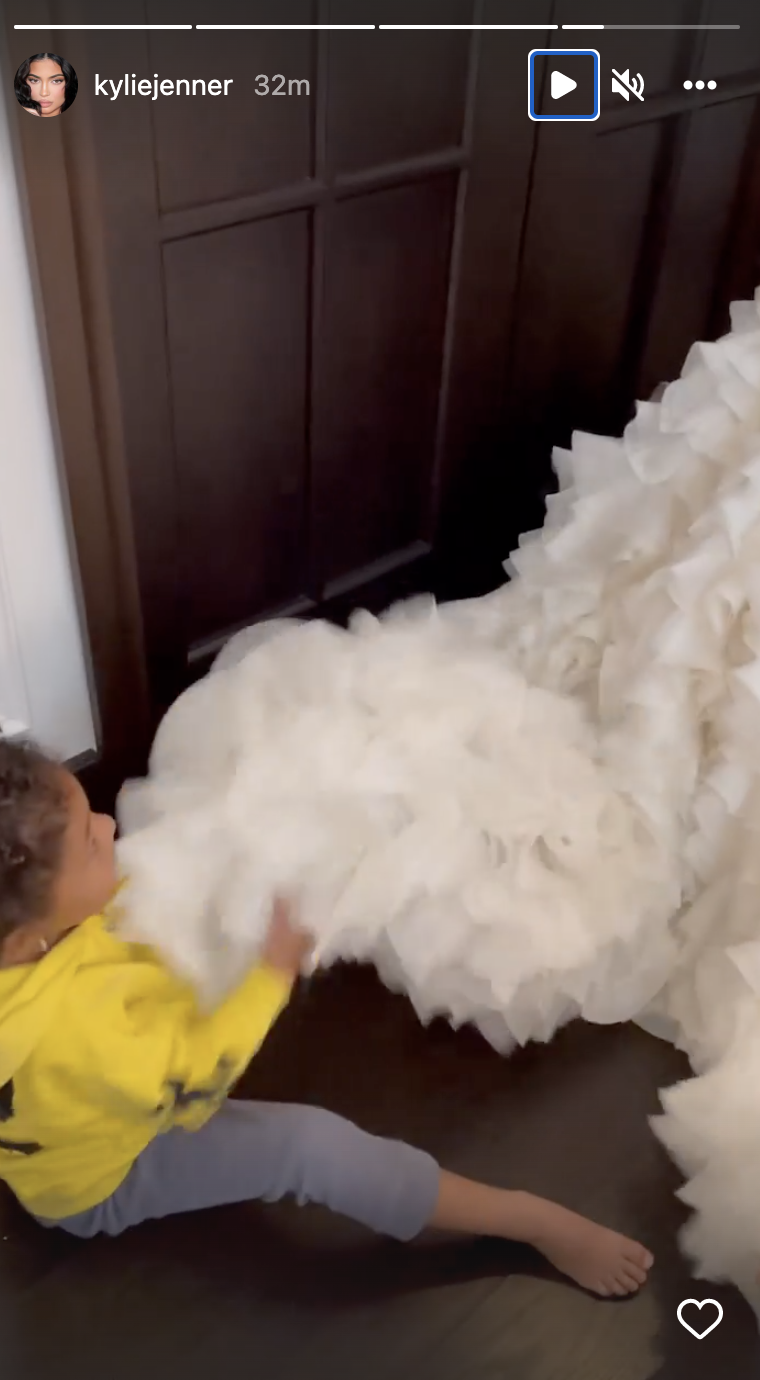 Stormi sitting on the ground and playing with the dress&#x27;s train