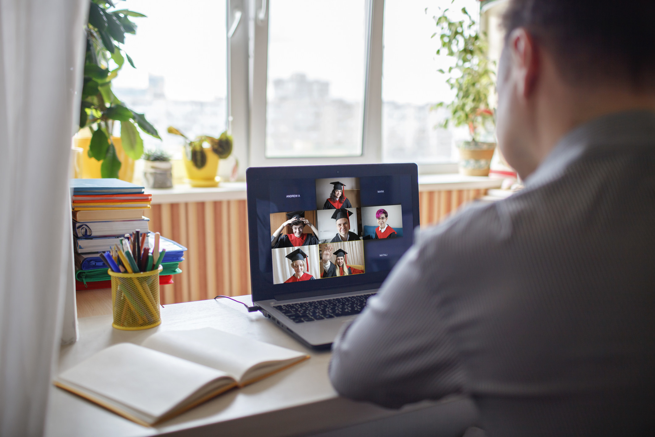 A person sits in front of a zoom call with several people wearing graduation caps