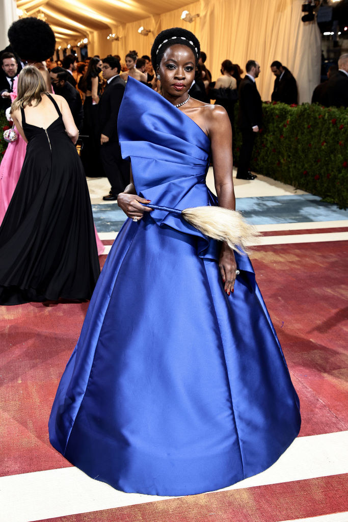 Danai Gurira in a gown with a big bell and holding a wand with a feathery end