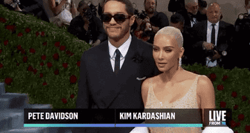 Pete Davidson and Kim Kardashian smiling together as paparazzi look on