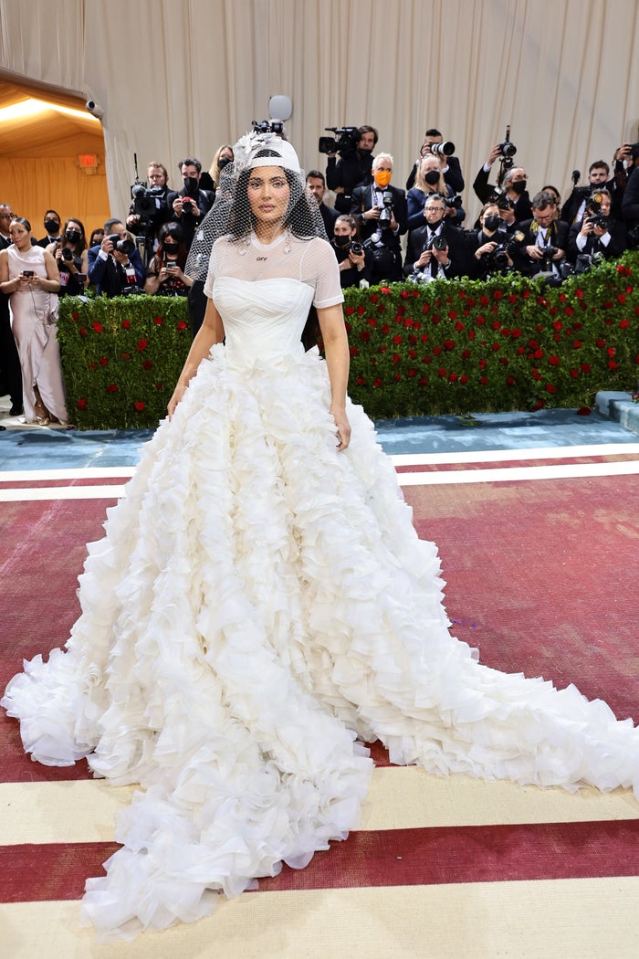 Kylie Jenner in a wedding dress with a billowy train and a baseball cap with a netted veil
