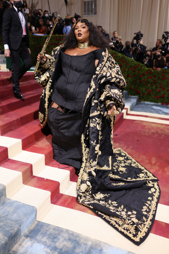 Lizzo wearing a long jacket with flowers embroidered in gold over a dark dress