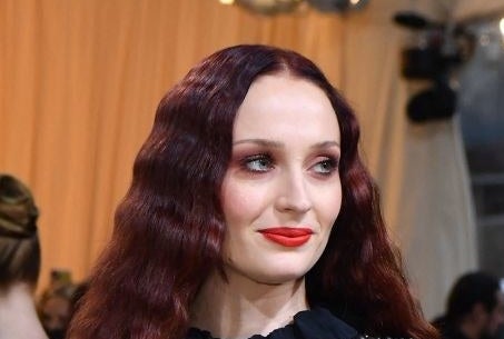 Sophie Turner with dark hair and makeup with reddish hues to match