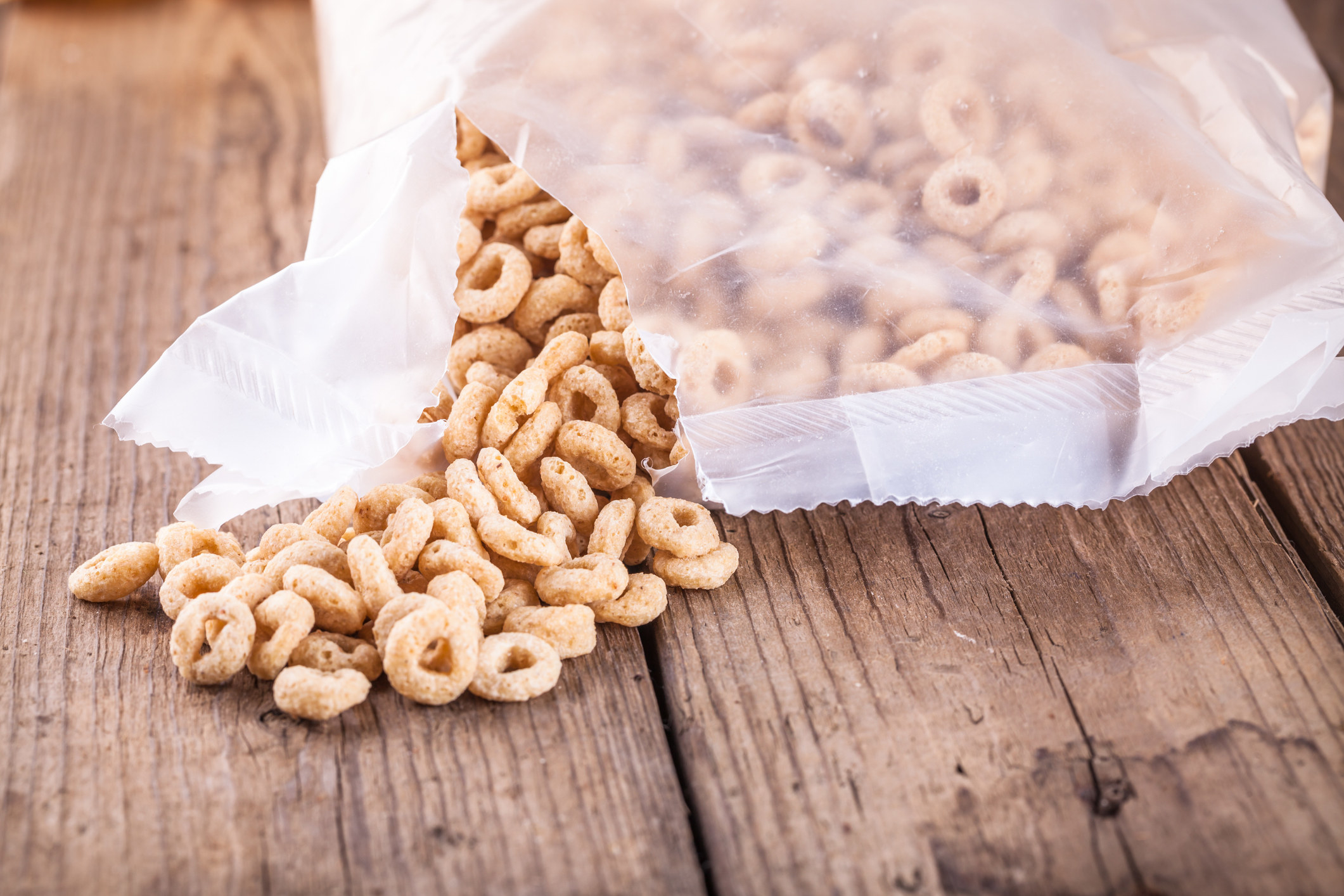 A ripped cereal bag with cereal spilling out onto the table.