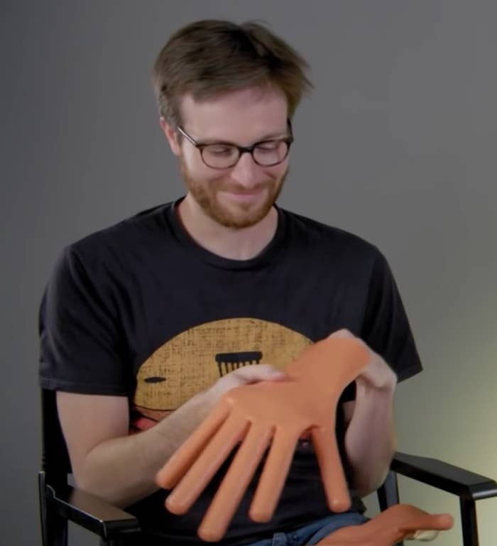 A man holds a glove with hot dogs instead of fingers