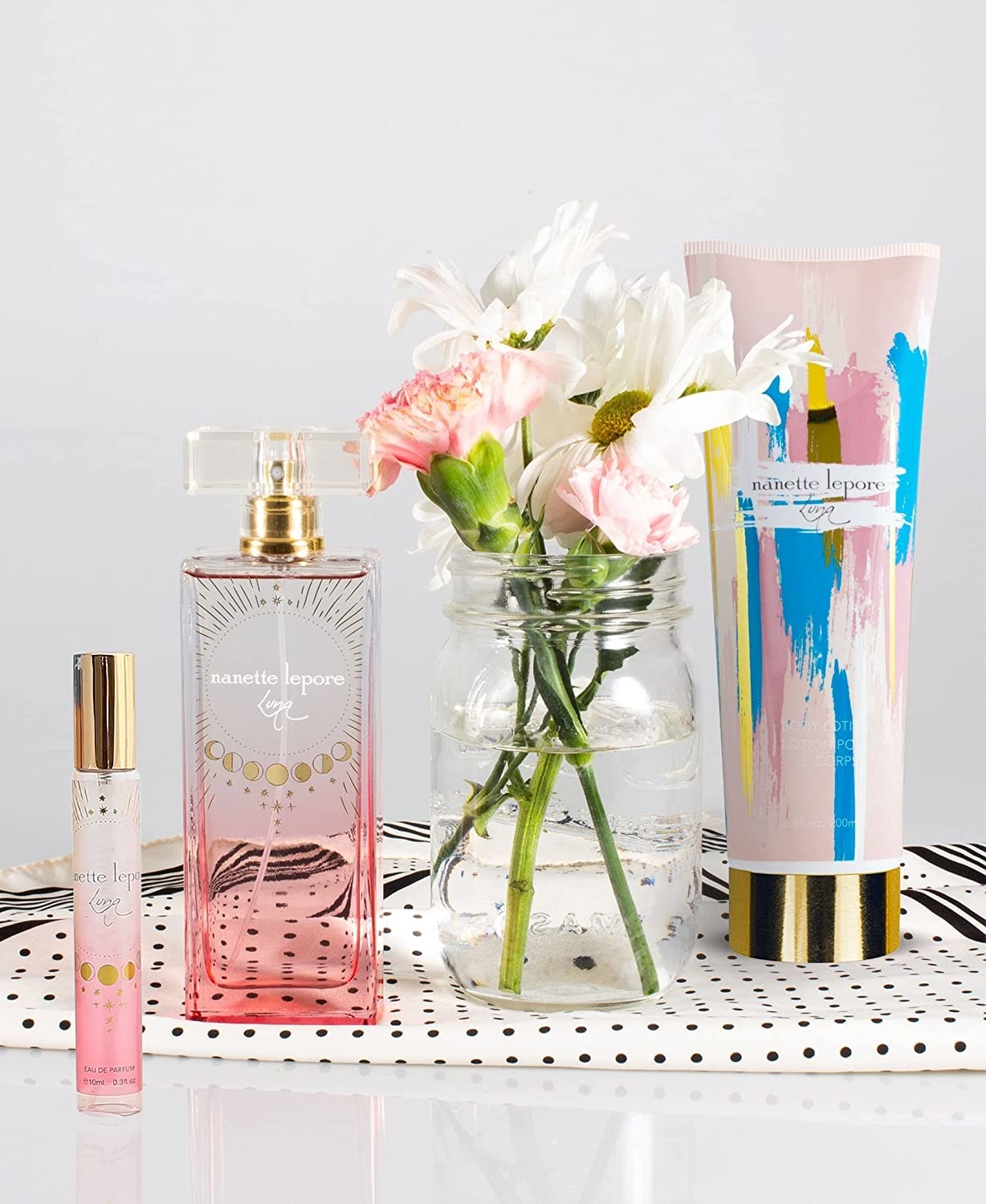 A set of three perfumes on a table. One bottle is small and pink, the other is large regtangular and pink and the other is in a pink tube with blue and yellow detailing
