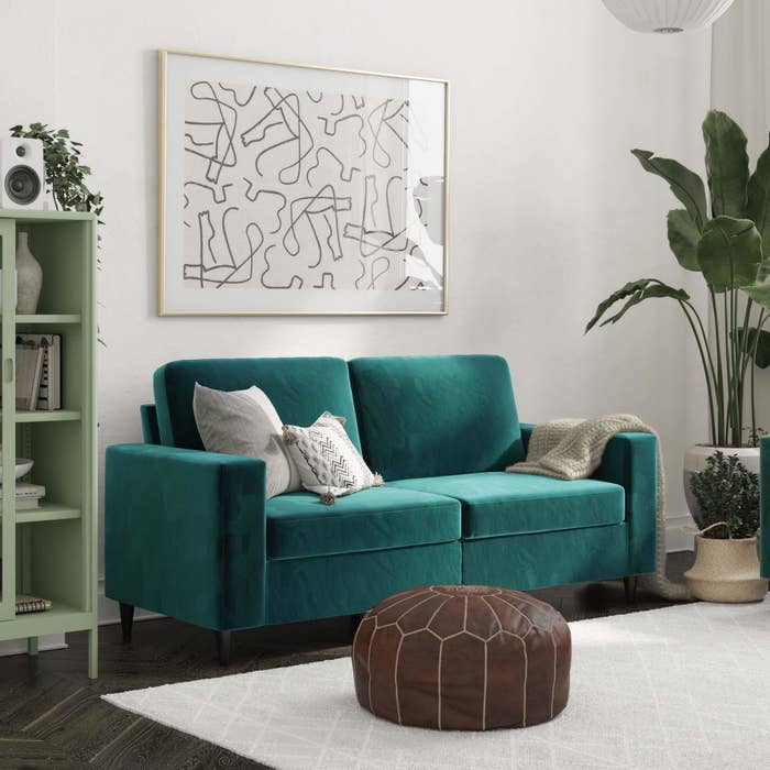 An image of a velvet green three-seater sofa with a sturdy wood frame and solid rubber wood legs with a black finish
