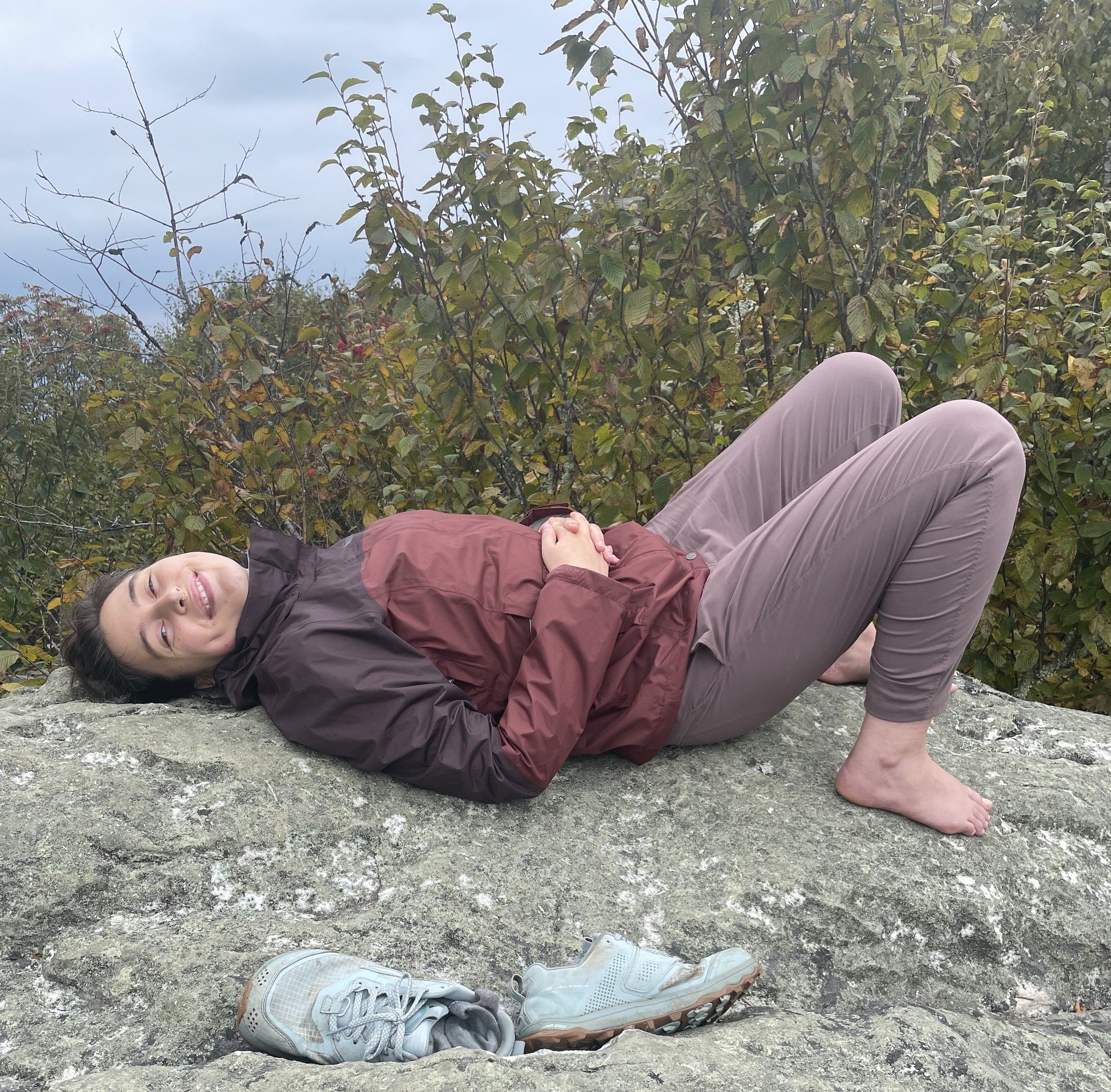 the writer laying down on a rock wearing the pants in light purple